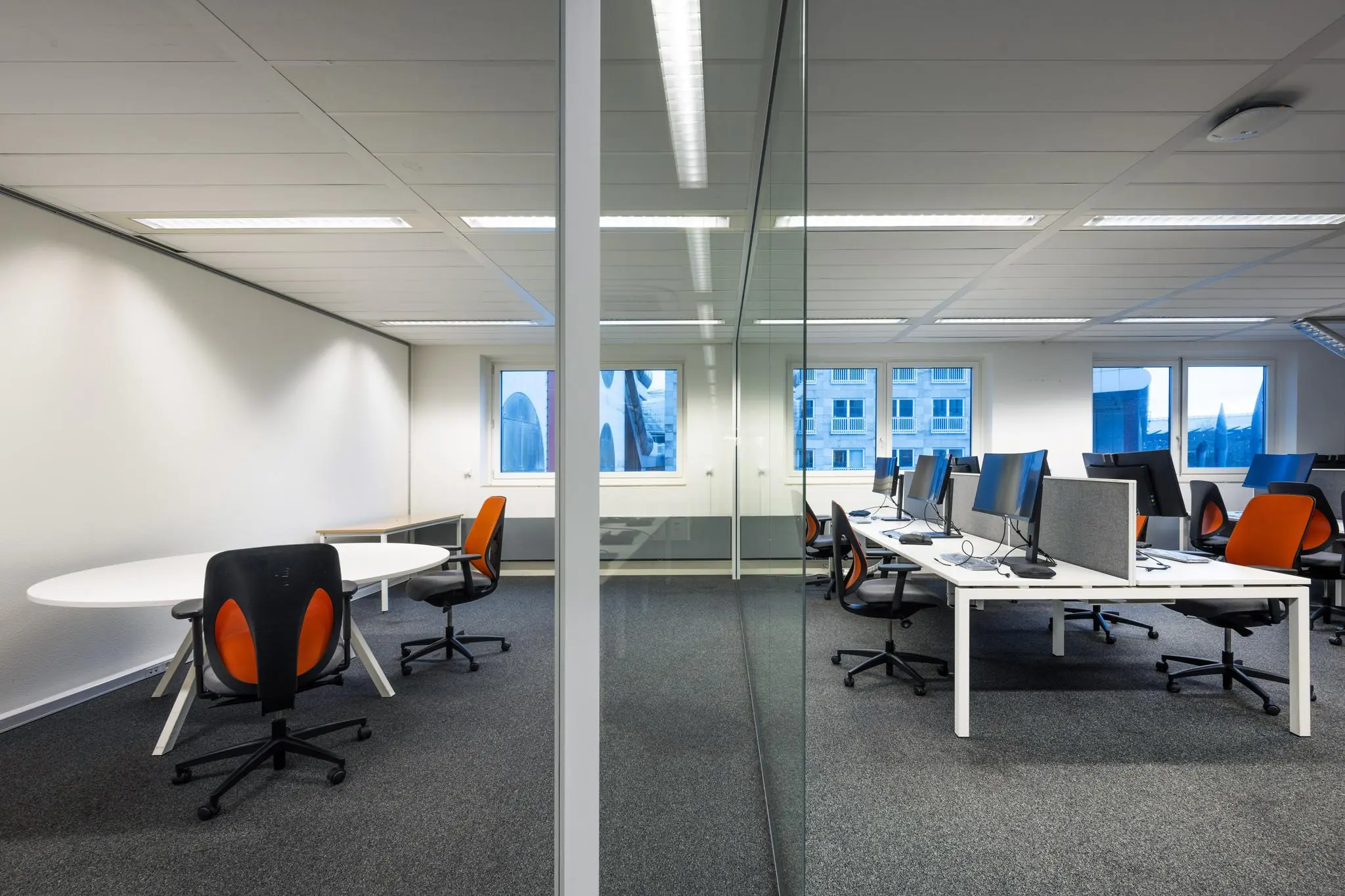 Modern kantoorinterieur aan de Johan Cruijff Boulevard met bureaus, computerschermen en oranje-zwarte bureaustoelen.